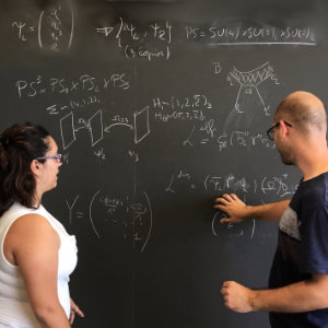 Foto eines Mannes und einer Frau, die vor einer Tafel voller Formeln und Skizze diskutieren.